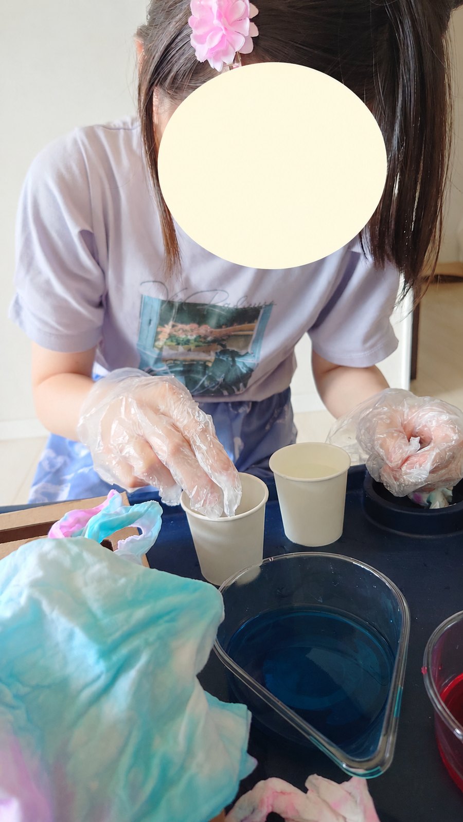 手袋をつけて紙コップで作業する様子。顔は保護のため加工